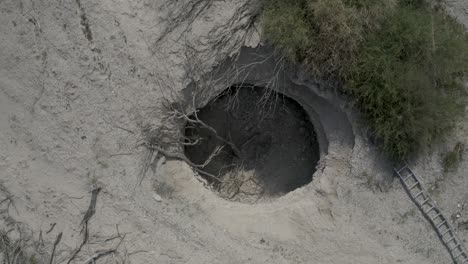 Aerial-Super-pull-out-top-down-shot-of-lost-wild-boar-laying-inside-sinkhole-in-Israel-desert,-drone-shot