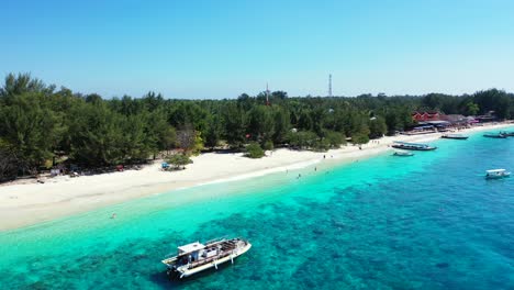 Touring-boats-anchoring-on-calm-clear-water-of-turquoise-sea-washing-white-sand-of-exotic-beach-in-front-of-holiday-hotels-full-of-people