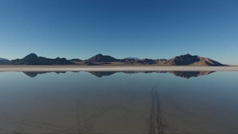 An-aerial-drone-shot-of-smooth-water-covering-the-Bonneville-Salt-Flats-reflects-distant-mountains