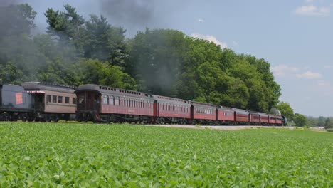 A-1910-Steam-Engine-with-Passenger-Train-Pulling-into-a-Station-Puffing-Black-Smoke-Along-the-Amish-Countryside-as-a-Second-Steam-Locomotive-Passes-on-a-Sunny-Summer-Day
