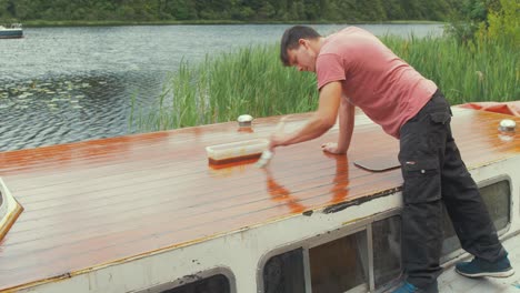 Carpenter-varnishes-roof-of-wooden-boat-with-brush-on-lake