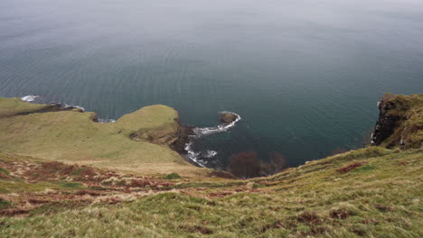 Schwenkaufnahme-Vom-Rand-Einer-Klippe-Aus-Wellen-Des-Atlantischen-Ozeans,-Die-An-Einem-Regnerischen-Und-Bewölkten-Tag-In-Schottland,-Isle-Of-Skye,-Die-Küste-Bespritzen