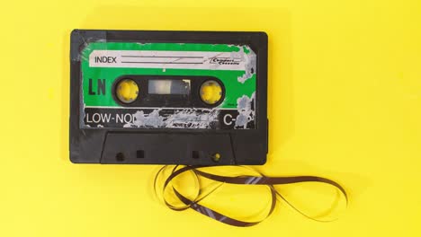 old-retro-cassette-tape-with-grunge-label-rewinding-pulled-tape-on-yellow-background-stop-motion