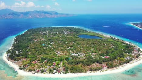 Circle-shape-of-tropical-island-with-trees-and-villas-for-vacation,-surrounded-by-turquoise-lagoon-and-blue-sea-on-a-shiny-morning-in-Indonesia