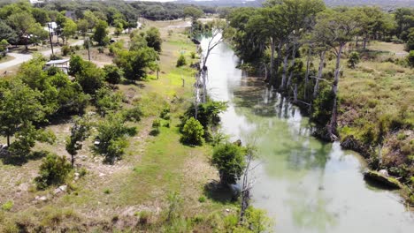 Pulling-away,-flying-back-above-river-towards-the-edge-of-the-riverbank-and-then-descending-to-land---Aerial-footage-of-the-Blanco-river-in-Wimberly,-TX