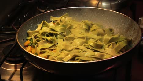 Adding-cooked-green-spinach-egg-pasta-on-the-top-of-vegetable-garnish-in-hot-pan-while-frying