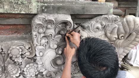 Hombre-Asiático-Esculpiendo-Patrones-Detallados-De-Un-Templo-Hindú-En-Las-Concurridas-Calles-De-Ubud,-Bali