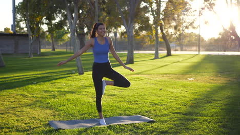 A-beautiful-young-woman-yogi-laughing-while-falling-over-and-losing-balance-in-a-one-legged-prayer-hands-yoga-pose-at-the-park-at-sunrise