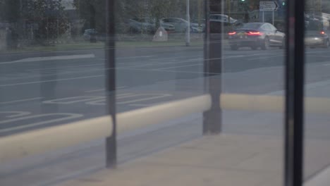 Point-of-view-of-urban-city,-traffic-at-dusk-through-bus-stop-windows