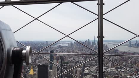 New-York-City-view-from-the-Empire-State-Building---gimbal-moving-through-the-fence-next-to-coin-operated-binoculars-at-the-observation-deck-on-a-sunny-summer-day-4K