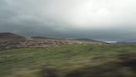 Bewegte-Aufnahme-Eines-Fahrzeugs-Mit-Sehr-Schnell-Vorbeifahrendem-Vordergrund-Und-Bergen-Und-Tälern-Im-Hintergrund-In-Wundervollem-Abendlicht-Mit-Schönen-Wolken-In-Schottland