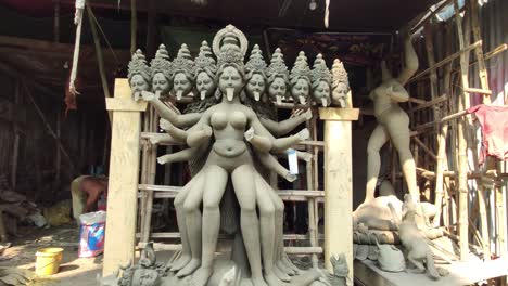 Unfinished-clay-idols-of-Indian-goddess-at-workshop,-people-working-behind,-smooth-camera-movement