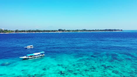 Touring-boats-floating-on-beautiful-blue-azure-sea-with-rocky-bottom-seen-through-clear-water-around-shore-of-tropical-islands-in-Bali