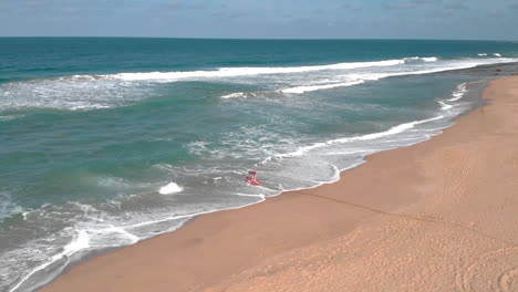 Aerial-shot-of-distant-person-heading-out-from-beach-with-red-kayak