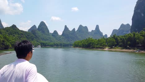 Chinese-man-tourist-admiring-stuning-karst-scenery-on-a-trip-on-the-magnificent-Li-river-from-Guilin-to-Yangshuo,-China