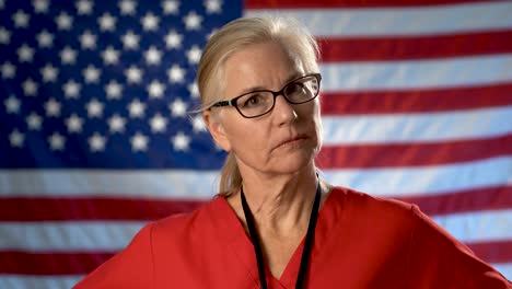 Portrait-of-a-nurse-walking-from-US-flag-to-foreground-and-showing-a-seriousness-and-disapproval