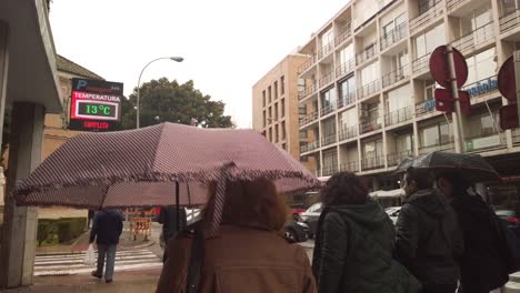 Walking-behind-people-with-umbrellas-on-rainy-day-in-Seville,-Spain,-SLOWMO