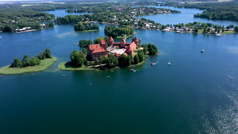 Luftaufnahme:-Rotierende-Aufnahme-Der-Burg-Trakai-In-Großer-Höhe-Mit-Booten-Und-Yachten,-Die-Auf-Dem-See-Um-Die-Insel-Der-Burg-Trakai-Kreisen,-Wobei-Die-Sonne-Lichtreflexion-Auf-Die-Oberfläche-Des-Sees-Wirft