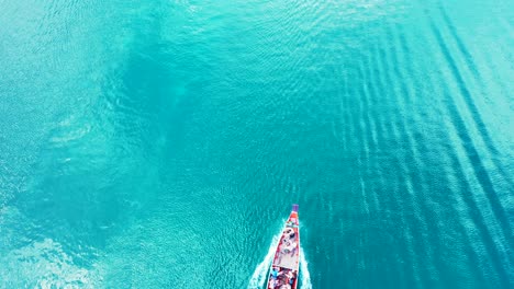 Long-tail-boat-sailing-on-vibrant-turquoise-water,-tracing-sea-surface-reflecting-sunlight-in-Thailand,-copy-space