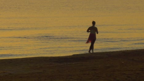 Woman-jogging-on-beach-at-daybreak-beside-calm-sea