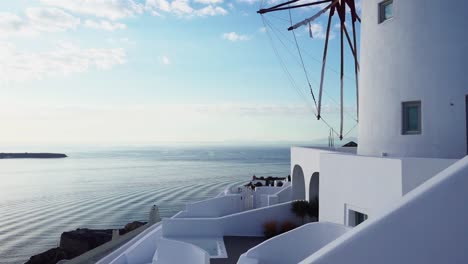 Weiße-Windmühle-Auf-Santorini-Mit-Kleinen-Wellen,-Die-Im-Hintergrund-über-Das-Meer-Rollen