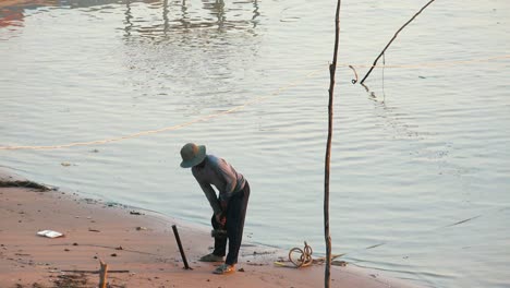 Medium-Exterior-Shot-of-Man-Hammering-Post-Into-the-Sand-With-a-Heavy-Hammer-Working-on-the-Shore-of-Lake-in-the-Daytime