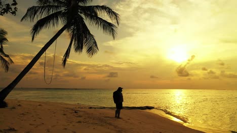 Silhouette-Eines-Backpacker-Mädchens-An-Einem-Exotischen-Strand-Mit-Palmen,-Die-Sich-über-Eine-Ruhige-Lagune-Bei-Goldenem-Sonnenuntergang-Auf-Den-Seychellen-Beugen