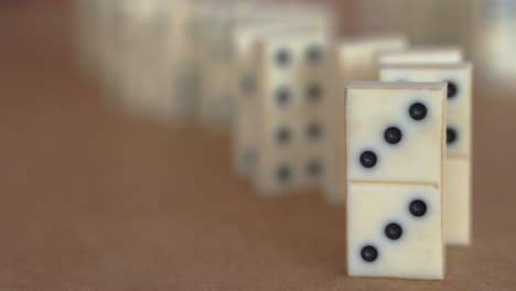 Close-up-view-of-row-of-white-dominoes-being-toppled-from-the-back-to-the-front-in-slow-motion