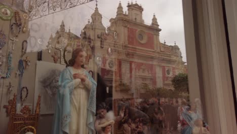 Virgin-Mary-statue-in-shop-window-with-church-in-reflection,-Seville,-Spain