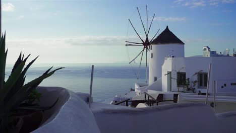 Wide-shot-of-a-windmill-overlooking-the-ocean-with-a-cactus-in-the-foreground,-Santorini,-Greece