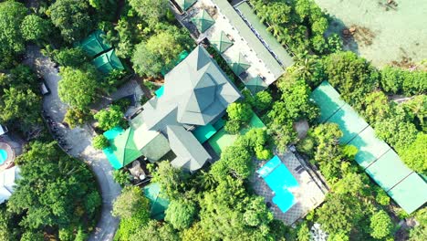Colorful-roofs-of-waterfront-resort-villas-through-green-trees-and-beautiful-gardens-on-shoreline-of-tropical-island,-Myanmar