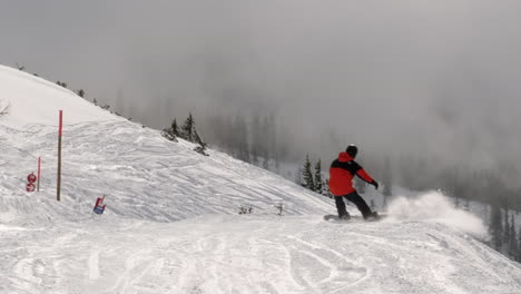 Toma-En-Gran-Angular-De-Una-Persona-Haciendo-Snowboard-Cuesta-Abajo-Usando-Equipo-De-Esquí-En-Una-Estación-De-Esquí-En-Wagrain-Con-Hermosas-Montañas-Cubiertas-De-Nieve-Y-Nubes-Dramáticas-En-El-Fondo