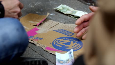 Men-playing-and-betting-on-a-card-game-on-an-alley,-Renminbi-money-is-placed-on-a-cardboard-box-Chongqing-China,-locked-close-up-shot