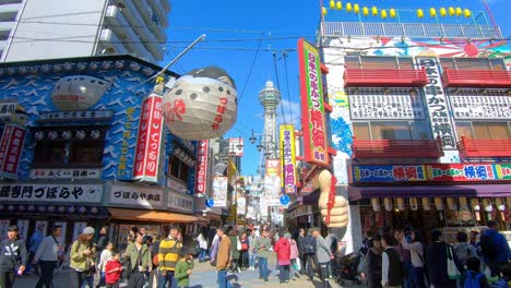 Tourists-walk-down-Osaka-streets-with-iconic-sightsee-Tsutenkaku-tower-in-background