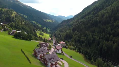 Aerial-view-of-a-small-village-with-church-in-the-mountain-area-with-houses-and-chalets,-Aerial-drone-flyover-shot