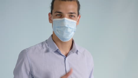 Smiling-young-man-puts-on-face-mask-and-raises-thumbs-up-turning-to-camera