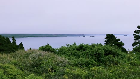 A-panning-view-of-cloud-covered-coastline,-over-brush-and-trees,-with-rock-islands