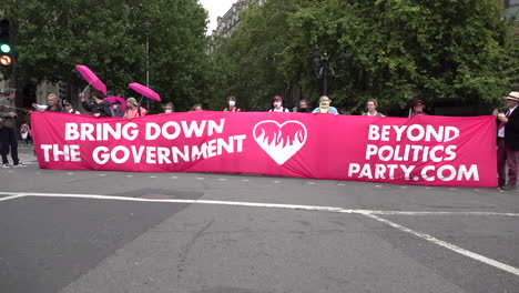 Beyond-Politics-Party-environmental-protestors-block-a-road-junction-on-Trafalgar-Square-with-a-large-bright-pink-banner-that-says,-“Bring-Down-The-Government”