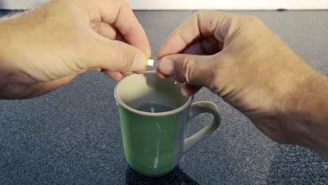 Person-öffnet-Pillenkapsel-Und-Gießt-Weißes-Pulver-In-Eine-Tasse