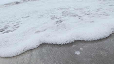 Foamy-sea-water-washing-up-on-a-sandy-beach-slow-motion