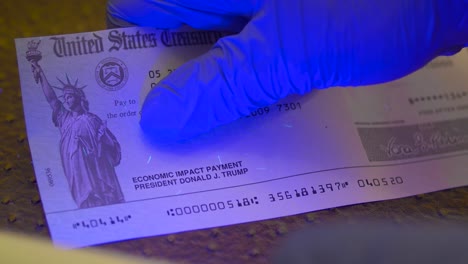 Stimulus-check-under-UV-light-showing-security-features-for-the-Coronavirus-economic-impact-payment-with-President-Trump's-name,-Close-up-shot