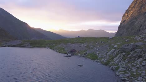 Luftaufnahme-Eines-Friedlichen-Bergsees-Bei-Sonnenuntergang-Mit-Dramatischem-Violettem-Und-Rotem-Himmel-über-Fernen-Gipfeln