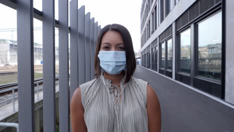Young-woman-standing-between-metal-grille-with-a-hygienic-respirator-mask-over-her-nose-and-mouth---Listen-to-music