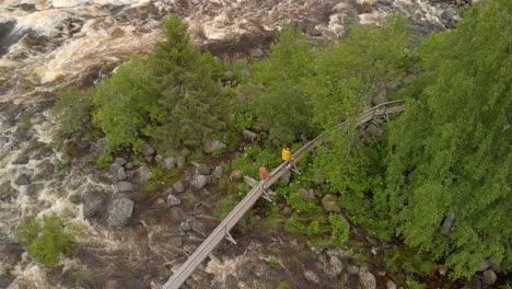 Aerial-footage-by-drone-of-two-men-walking-over-small-bridge-over-kalix-rapid