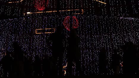 Menschen,-Die-Nachts-In-Der-Weihnachtszeit-In-Der-Stadt-Funch,-Portugal,-In-Silhouette-Vor-Einem-Riesigen-LED-beleuchteten-Weihnachtsbaum-Laufen-Und-Laufen