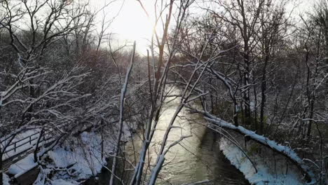 Rising-aerial-shot-over-wintry-creek-and-forest-in-Michigan,-USA