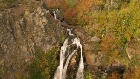 Cinematic-aerial-shot-of-a-waterfall-and-revealing-an-autumnal-woodland-in-Patagonia,-Argentina