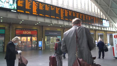 Man-stands-checking-the-train-times-at-Kings-Cross-Station-during-the-coronavirus-pandemic-in-London,-UK