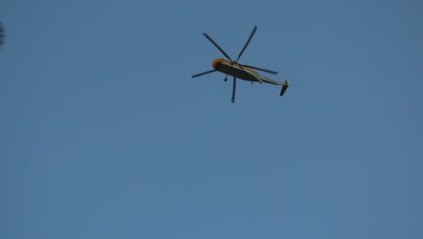 A-firefighting-helicopter-flies-directly-overhead-searching-for-water-for-nearby-forest-fire-wildfire-and-disappears-behind-trees