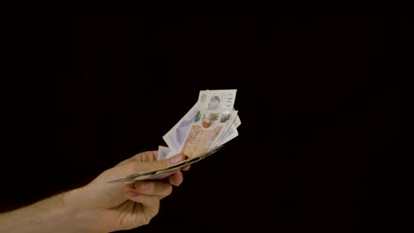 Hand-waving-a-messy-stack-of-cash-money-against-a-black-background-in-slow-motion-wide-shot
